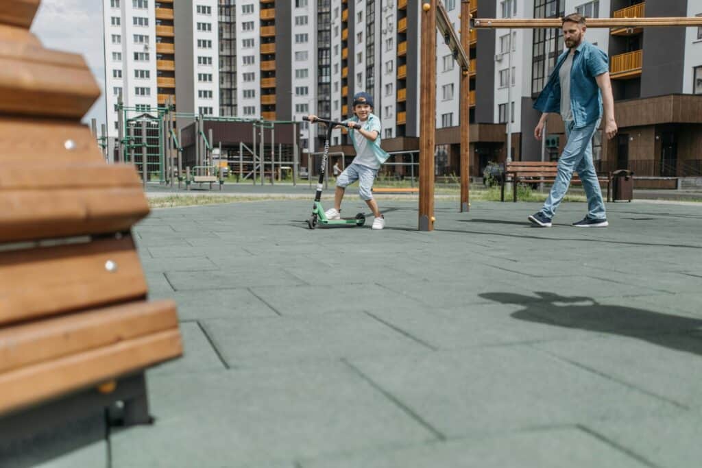 A father and son in a playground surrounded by apartment buildings