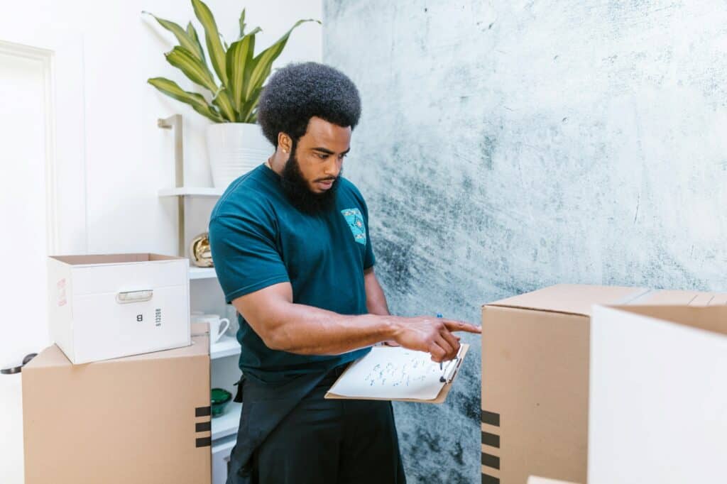 A professional mover is checking the inventory and is surrounded by boxes while holding a clipboard in the concept of man and van in Wood Green.