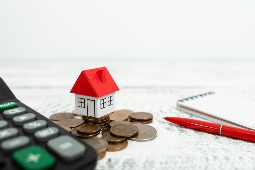 House figurine, calculator, coins, pen, and notebook in the concept of 'how to save money when moving to Wood Green'.