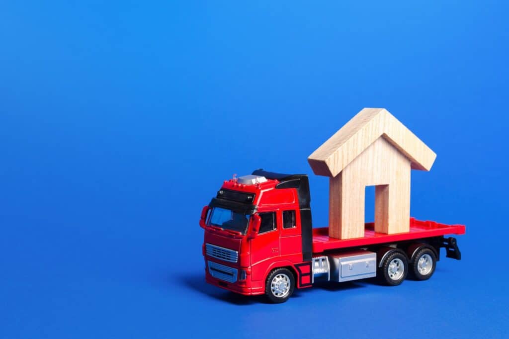 A toy truck carrying a house figurine in the concept of a moving company