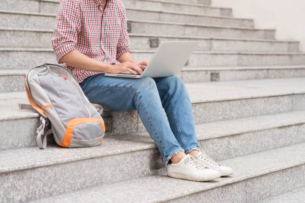 A male student using the laptop and sitting on the school's staircase