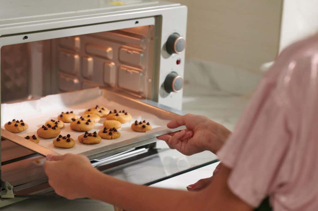 A woman placing a try of cooking dough into the oven